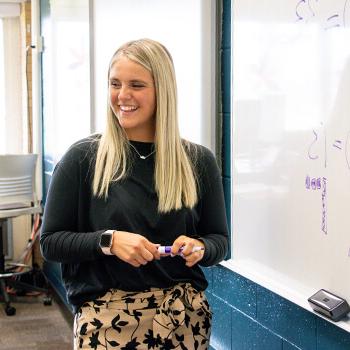 Concordia alum teaches her mathematics class, using a purple dry erase marker on a whiteboard.